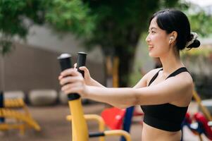 Young asian athletic sportswoman 30s wearing sportswear listening relaxing music while working out exercise equipment outdoor in park. Healthy lifestyle concept photo