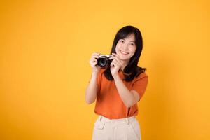 Young lady holding a camera isolated on yellow background, conveying the excitement of a travel adventure. photo