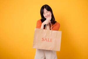 Get ready for a shopping adventure filled with love and surprises. Young woman in her 30s exudes happiness while presenting her purchases and best bargains isolated on yellow background. photo