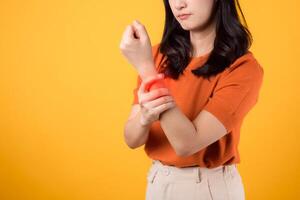 Young woman 30s standing with a sore wrist isolated on yellow background, showcasing arthritis pain. Portrait of a person suffering from wrist ache. photo