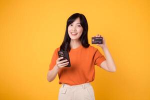 Dynamic Asian woman in her 30s, using smartphone and showing credit card on yellow background. Efficient online shopping. photo