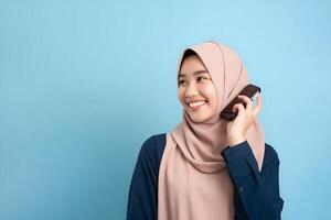 ai generado linda joven asiático niña en hijab participación un teléfono inteligente en frente de un vibrante azul antecedentes foto