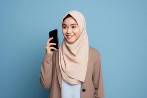 ai generado linda joven asiático niña en hijab participación un teléfono inteligente en frente de un vibrante azul antecedentes foto