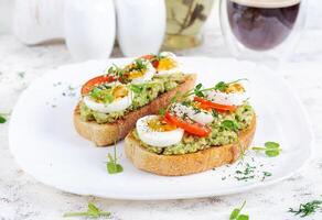 Delicious toast with avocado, boiled egg, tomatoes and microgreen on a white plate. Healthy eating, breakfast. Keto diet food. Trendy food. photo