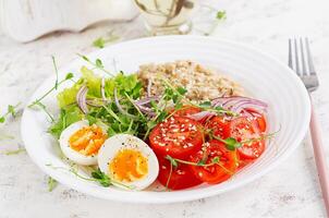 Breakfast oatmeal porridge with boiled eggs and fresh vegetables. Healthy balanced food. Trendy food. photo