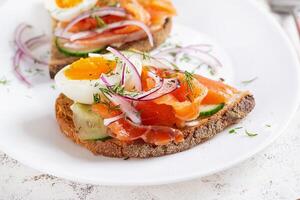 Delicious toast with salmon, boiled egg, cucumber and cream cheese on a white plate. Healthy eating, breakfast. Keto diet food. Tasty food. photo