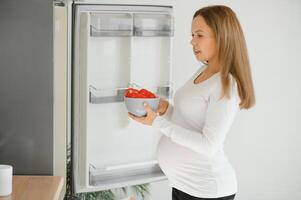 embarazada mujer a hogar en el cocina abre el refrigerador foto