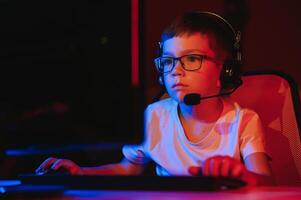 Child online broadcasts computer game, boy streams in headphones on rgb lighting background photo