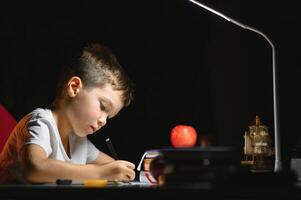 Boy learn lessons in the home setting at the table in the light of a table lamp. photo