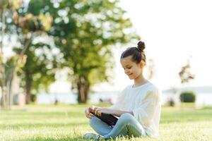 Child with tablet pc outdoors. Little girl on grass with computer photo