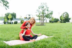 Mother and daughter doing yoga exercises on grass in the park at the day time photo