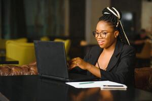 enfocado hembra oficina trabajador utilizando computadora en café tienda. africano americano negocio mujer trabajando en ordenador portátil en café y mirando lejos. Internet tecnología concepto foto