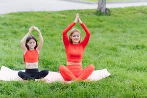 Mother and daughter doing yoga exercises on grass in the park at the day time photo