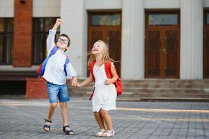 Happy children go back to school. Pupil of primary school go study with backpack outdoors. Kids go hand in hand. Beginning of lessons. First day of fall. Boy and girl from elementary student. photo