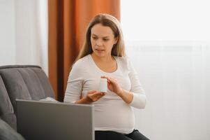 Pregnant woman video chatting with doctor on laptop. Professional medical online consultation concept. photo