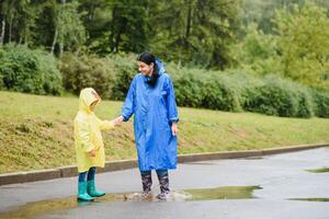 mamá y hijo en impermeables tener divertido juntos en el lluvia. concepto de familia vacaciones y contento infancia. foto