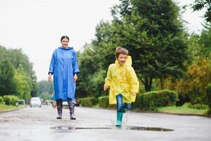 Mother and child, boy, playing in the rain, wearing boots and raincoats photo