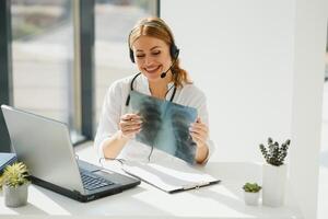 joven hembra médico hablando a paciente en línea desde médico oficina. médico consultante cliente en vídeo charla ordenador portátil a hospital. foto