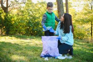 Smiling boy picking up trash in the park with his mother. Volunteer concept. photo