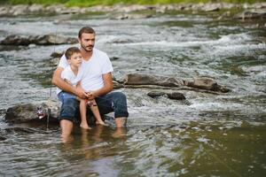 un padre enseñando su hijo cómo a pescado en un río fuera de en verano Brillo Solar foto