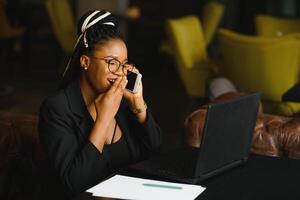 Young beautiful Afro-American businesswoman smart phone and smiling while working in cafe photo