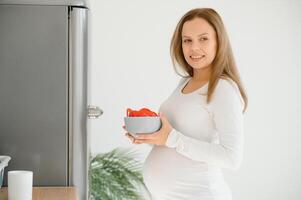 embarazada mujer a hogar en el cocina abre el refrigerador foto