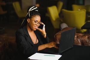 Young beautiful Afro-American businesswoman smart phone and smiling while working in cafe photo