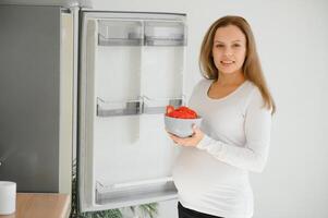 embarazada mujer a hogar en el cocina abre el refrigerador foto