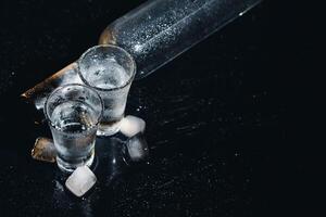 Close-up view of bottle of vodka with glasses standing on ice on black. photo