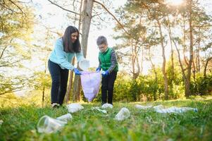 Smiling boy picking up trash in the park with his mother. Volunteer concept. photo