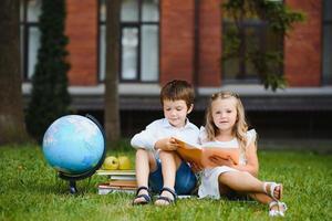 Schoolgirl sitting on green grass and talking to her friend they preparing for the lessons together before school photo