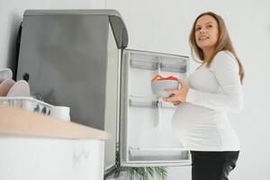 embarazada mujer a hogar en el cocina abre el refrigerador foto