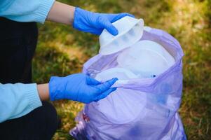 mano pone el plastico escombros en el basura bolso en el parque foto