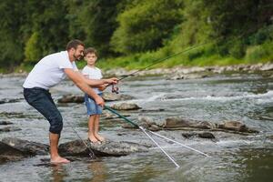 un padre enseñando su hijo cómo a pescado en un río fuera de en verano Brillo Solar foto