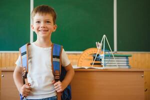 Back to school. Funny schoolboy sitting at a table with books in a school classroom. photo