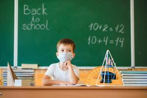 Schoolboy in the classroom in a protective mask. The concept of schooling during the epidemic photo