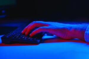 Close-up On Gamer's Hands on a keyboard, Actively Pushing Buttons, Playing MMO Games Online. Background is Lit with Neon Lights. photo