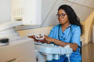 sonriente africano mujer médico con ultrasonido escáner en mano, trabajando en moderno ultrasonido exploración máquina en ligero habitación en clínica. retrato de 4d ultrasonido exploración máquina operador foto