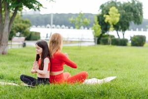 Mother and daughter doing yoga exercises on grass in the park at the day time. People having fun outdoors. Concept of friendly family and of summer vacation. photo