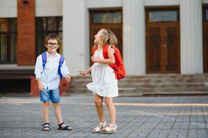 Happy children - boy and girl with books and backpacks on the first school day. Excited to be back to school after vacation. Full length outdoor portrait. photo