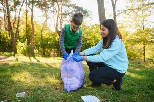 Smiling boy picking up trash in the park with his mother. Volunteer concept. photo
