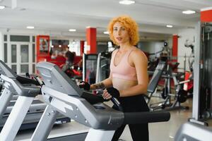 Attractive young sports woman is working out in gym. Doing cardio training on treadmill. Running on treadmill. photo