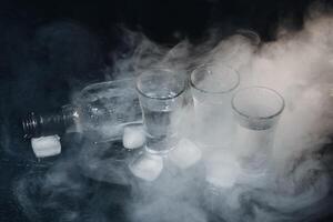 Close-up view of bottle of vodka with glasses standing on ice on black. photo