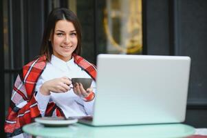 beautiful and happy woman sits with a laptop in a cafe on the street and drinks coffee. freelance work. outdoor meetings. photo