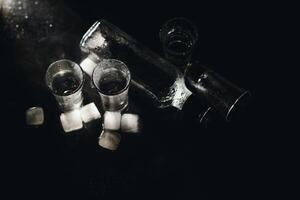 Close-up view of bottle and glasses of vodka standing isolated on black. photo