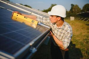 Construction worker connecting photo voltaic panel to solar system using screwdriver on shiny surface and lit by sun green tree background. Alternative energy and financial investment concept.