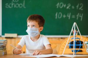 pequeño colegial vistiendo protector máscara en aula. concepto de epidemia foto