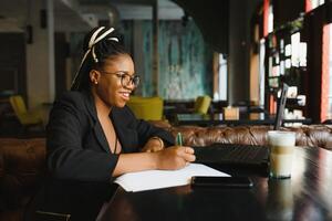 hermosa afro americano niña en casual ropa es utilizando un ordenador portátil y sonriente mientras sentado en café foto