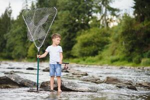 cute boy in white T shirt fishing in the river and has fun, smiles. vacation with kids, holidays, active weekends concept photo