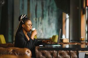 satisfecho africano niña utilizando ordenador portátil a cafetería, trabajando en línea, Copiar espacio foto